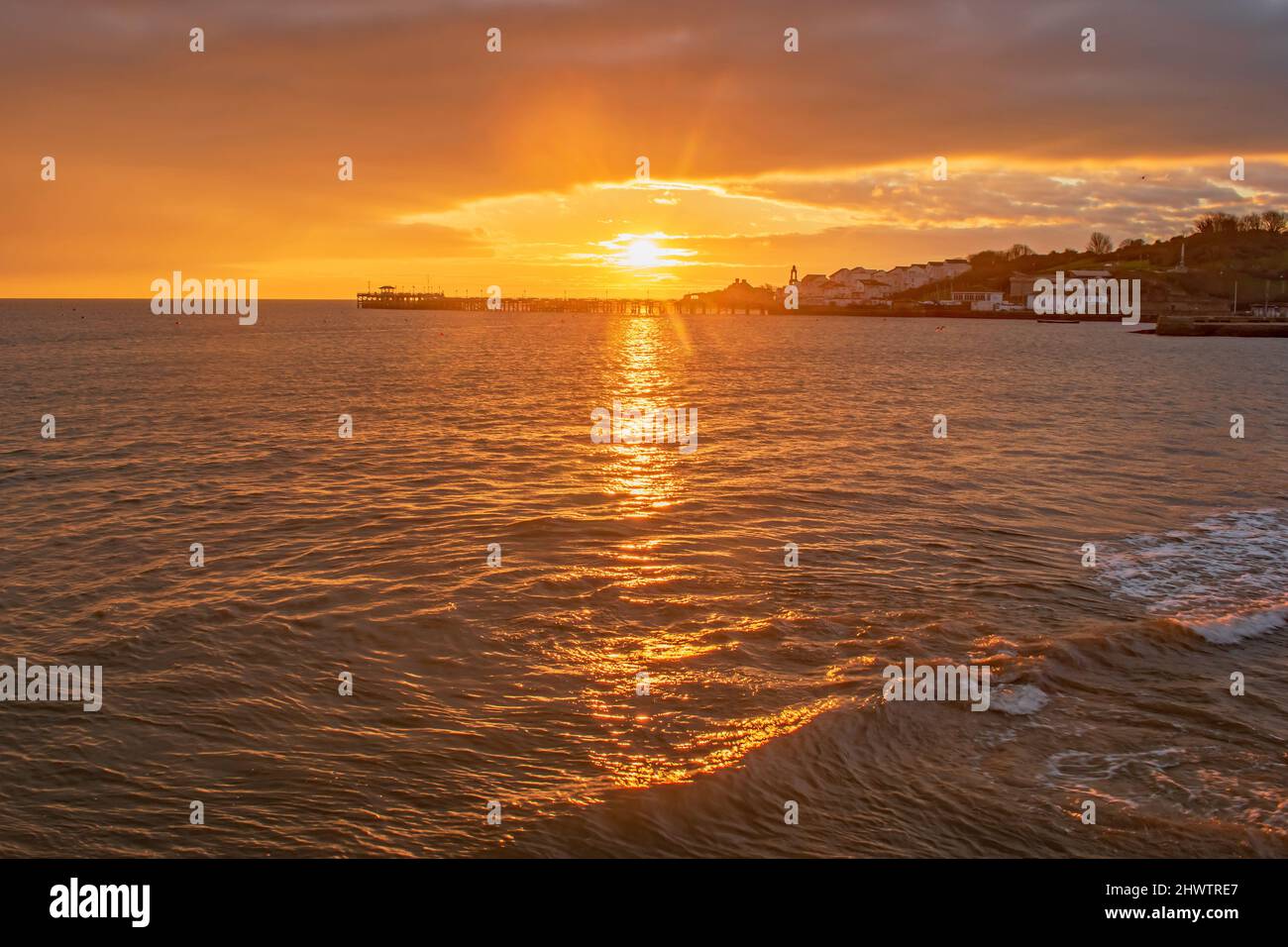 A Golden Orange sunrise burst over the old Swanage pier spreading golden rays Stock Photo