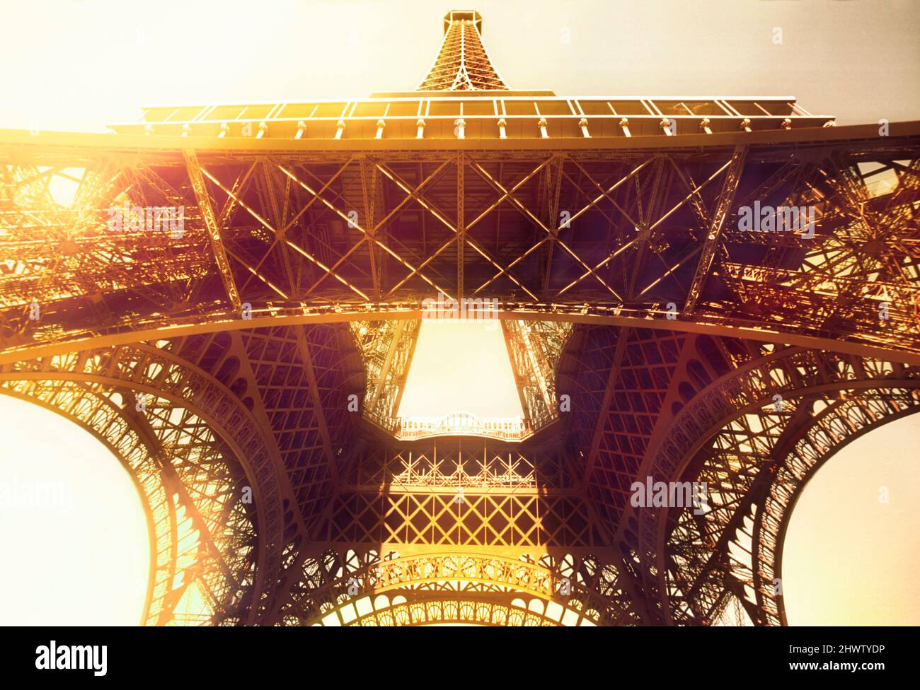 Eiffel Tower, Paris, dawn. Looking up at the landmark iconic wrought iron lattice monument and glaring sunlight. Belle Epoque architecture France Stock Photo