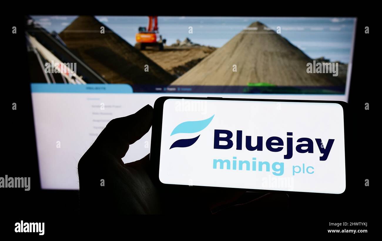 Person holding cellphone with logo of British company Bluejay Mining plc on screen in front of business webpage. Focus on phone display. Stock Photo