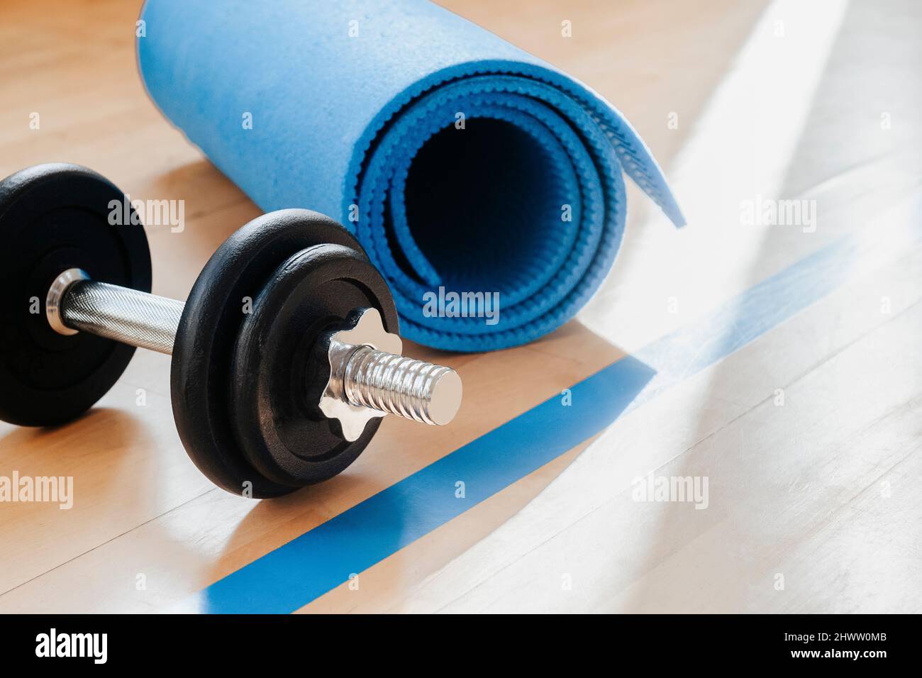 Blue color dumbbells and gym mat on wooden surface. Concept of rehabilitation and sport training equipment Stock Photo