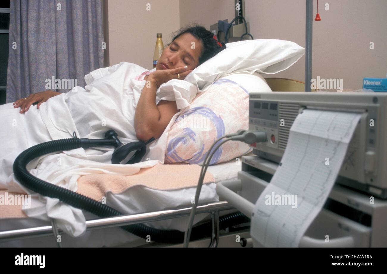 labouring hispaniic woman asleep in hospital bed with gas & air reliever by her side Stock Photo
