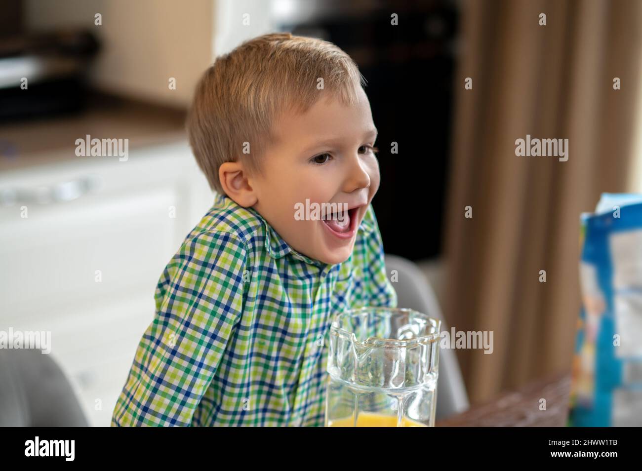 Kid with his mouth open leaning on the kitchen table Stock Photo