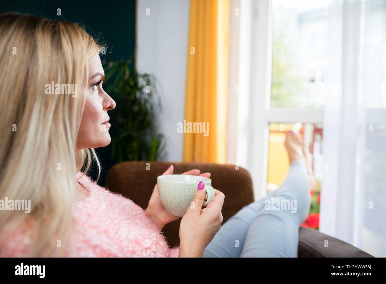 A young woman holds a cup and looks ahead. Stock Photo