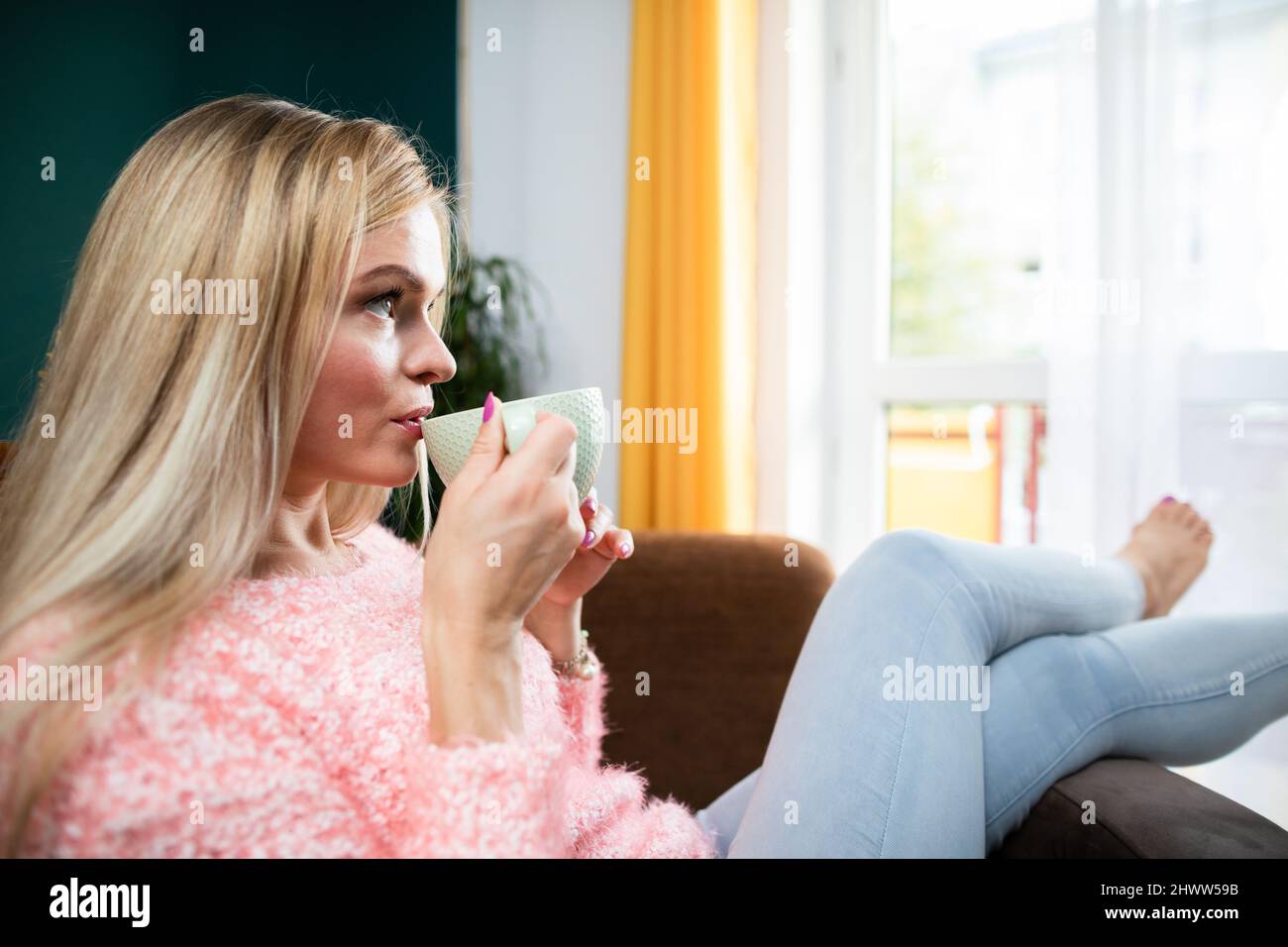 A young woman drinks coffee while sitting in the living room. Stock Photo