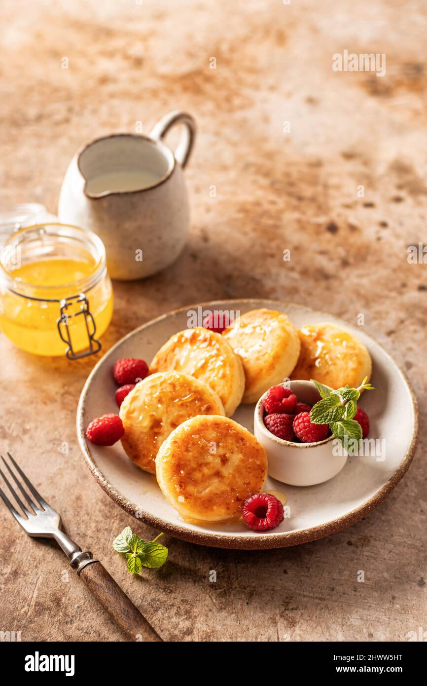 Cottage cheese pancakes, syrniki with honey and fresh raspberry on ceramic plate on textured background Stock Photo