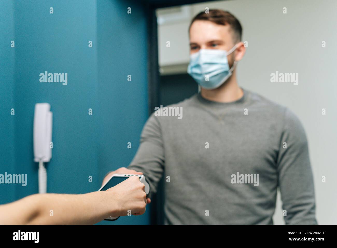 Selective focus of courier male wearing protective face mask giving POS wireless terminal to making contactless payment via credit card Stock Photo