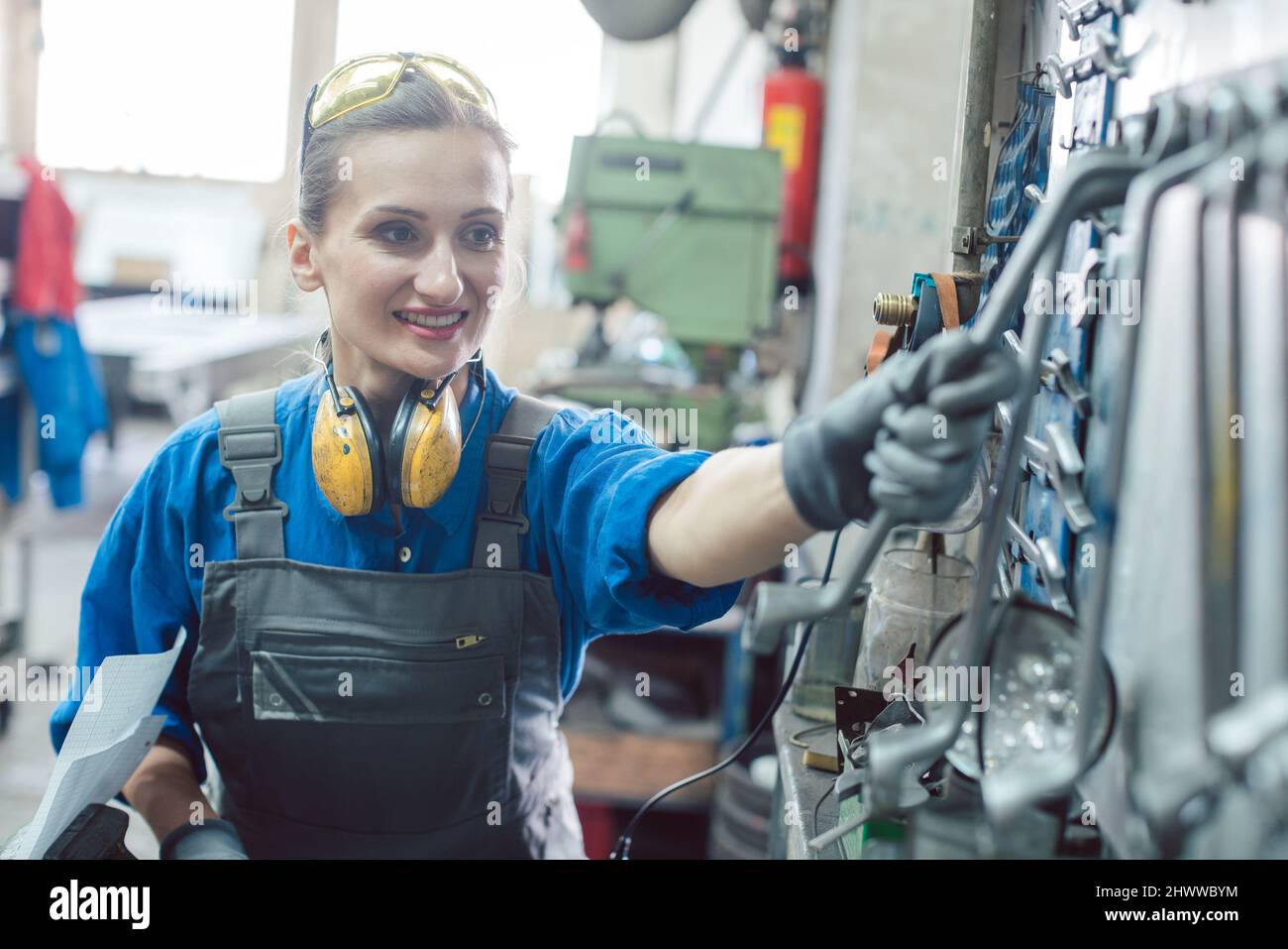 Woman in factory grabbing tool from wall mount Stock Photo
