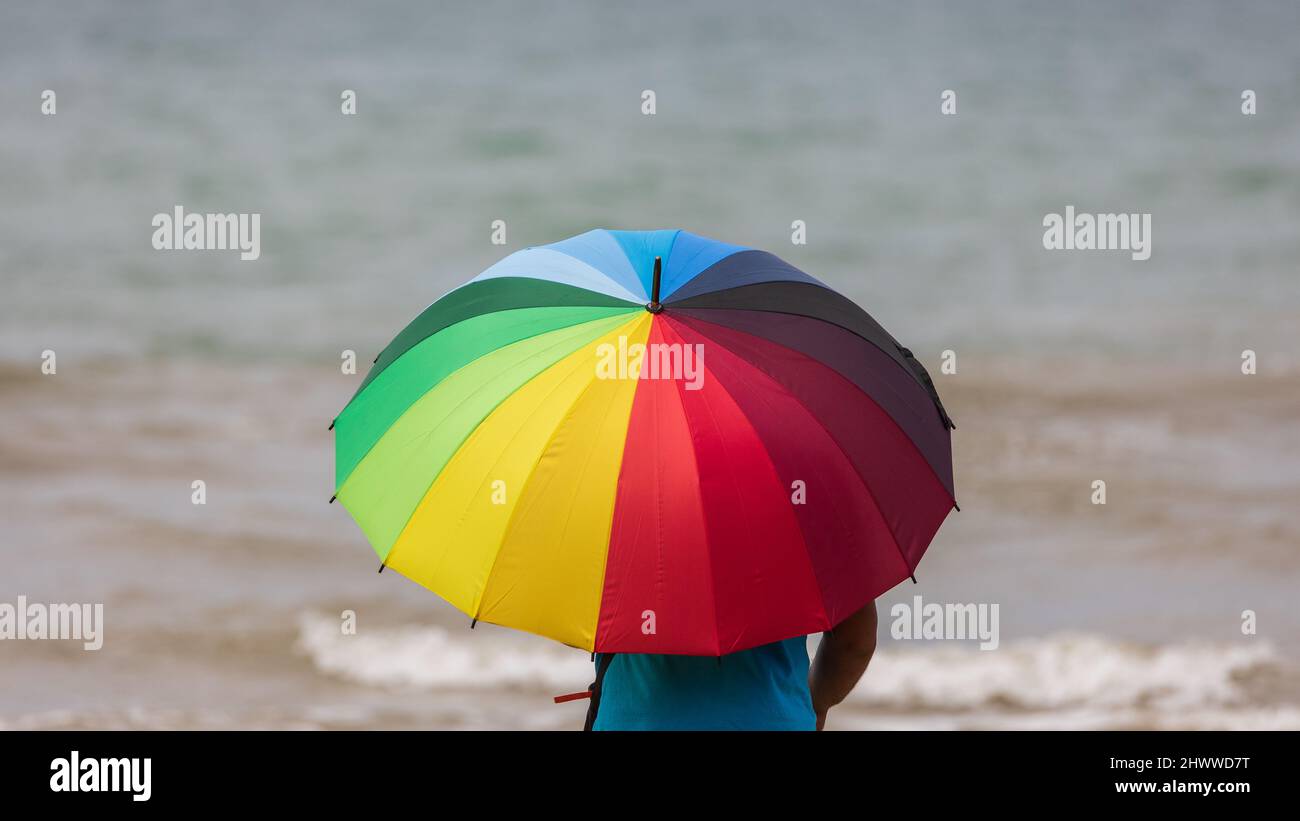 Man hold a rainbow color umbrella during sunny day at beach Stock Photo ...