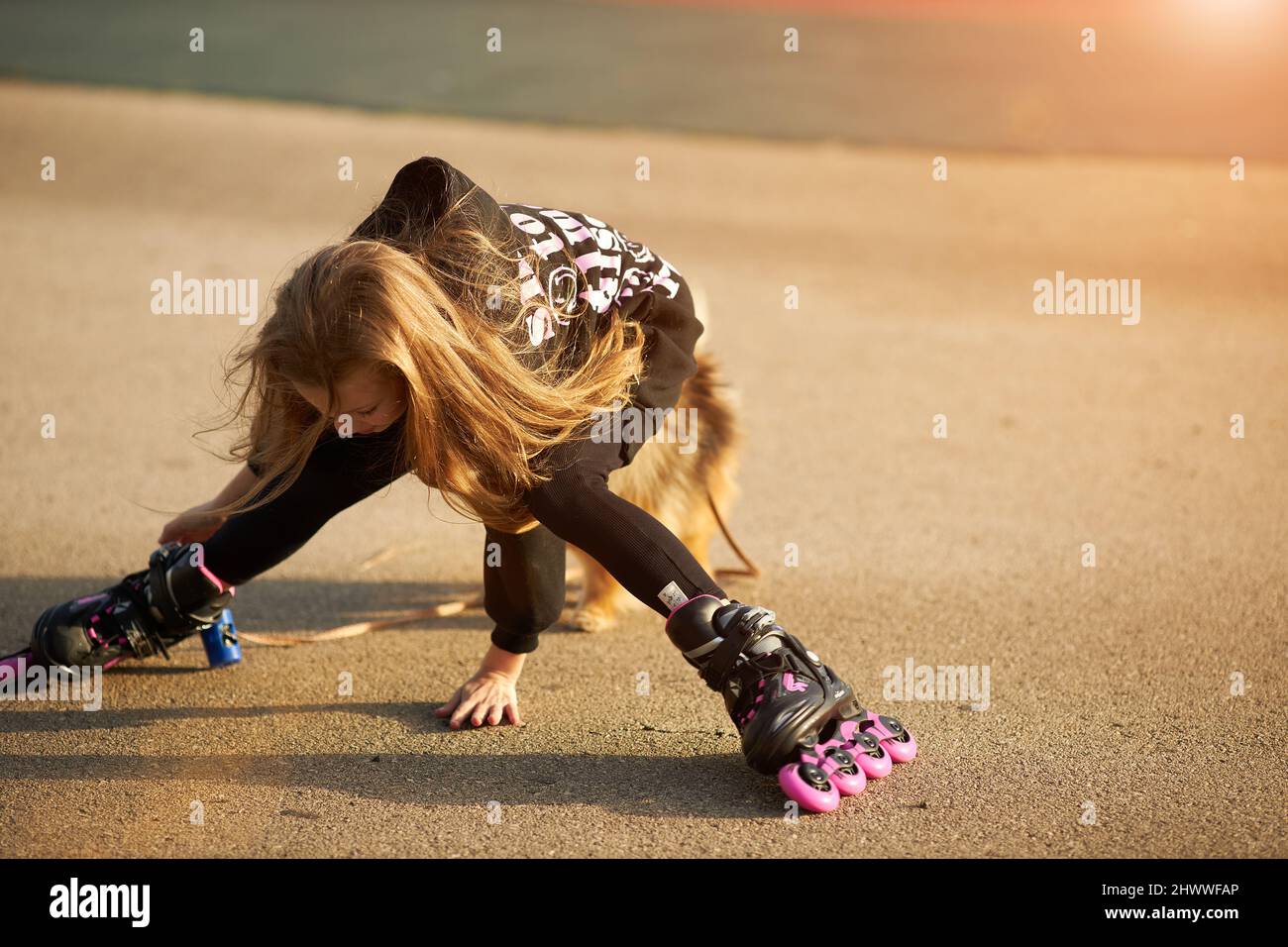 Cute child girl riding on roller skates and fall down in the park Stock Photo