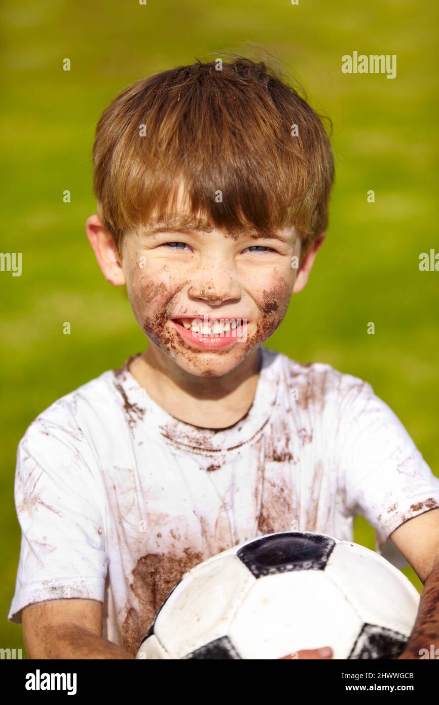 Want to play. Portrait of a muddy little boy holding a soccer ball. Stock Photo