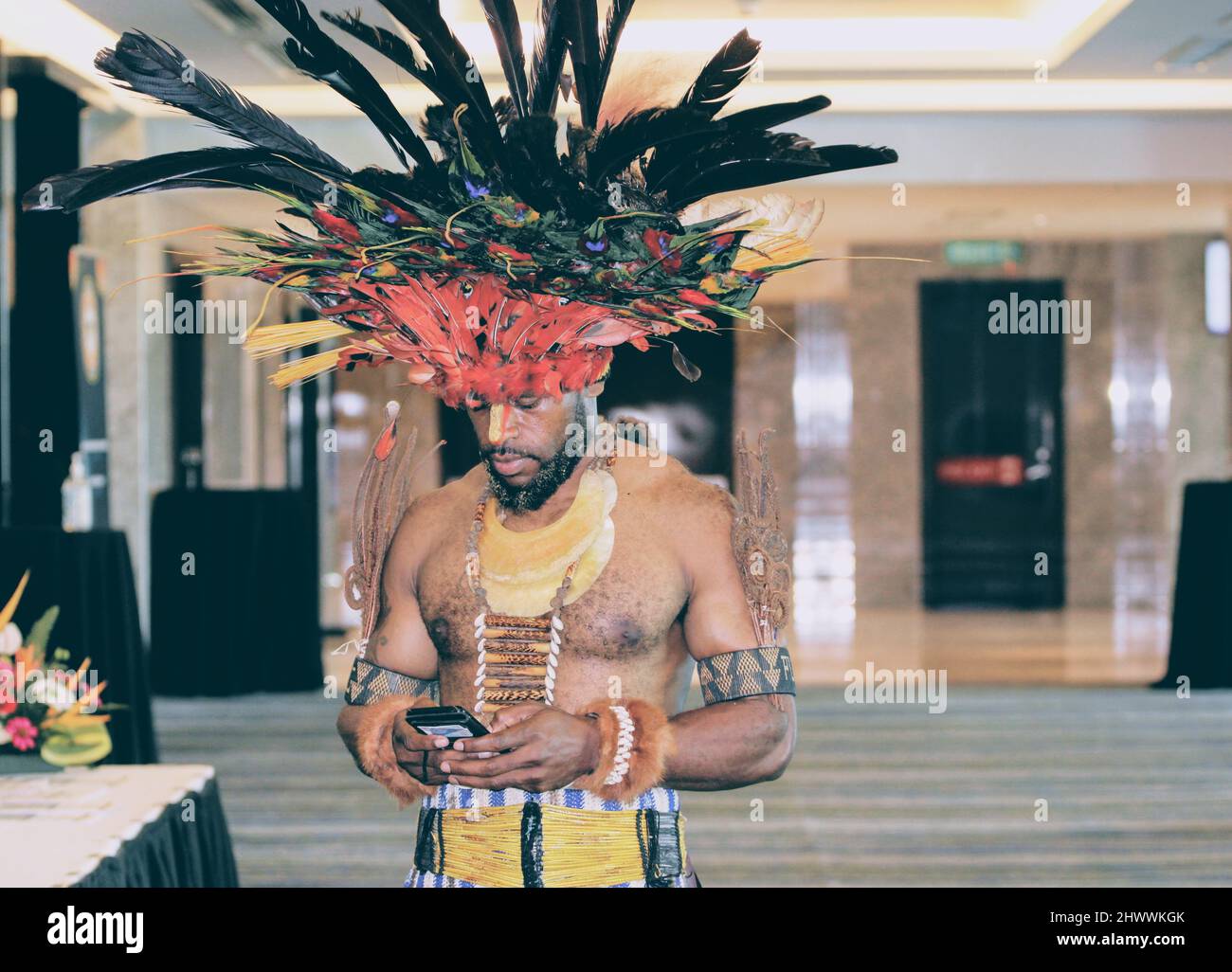 A Papua New Guinean highlander in traditional attire using a smartphone at The Stanley Hotel & Suites' Kokoda Ballroom. Stock Photo