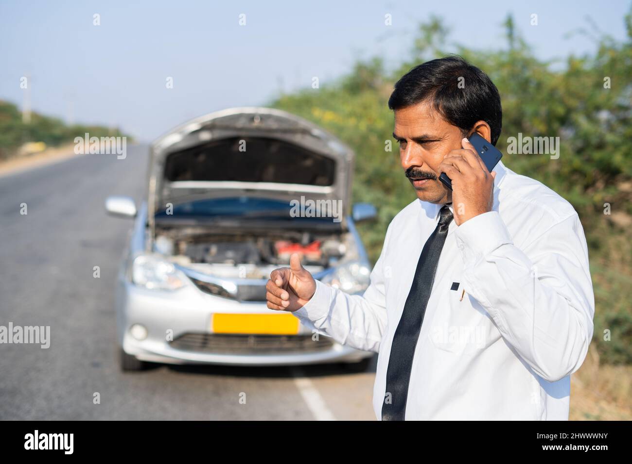 worried Businessman talking on mobile phone with car mechanic while car breakdown at highway road - concept of mobile car repair, assistance and Stock Photo
