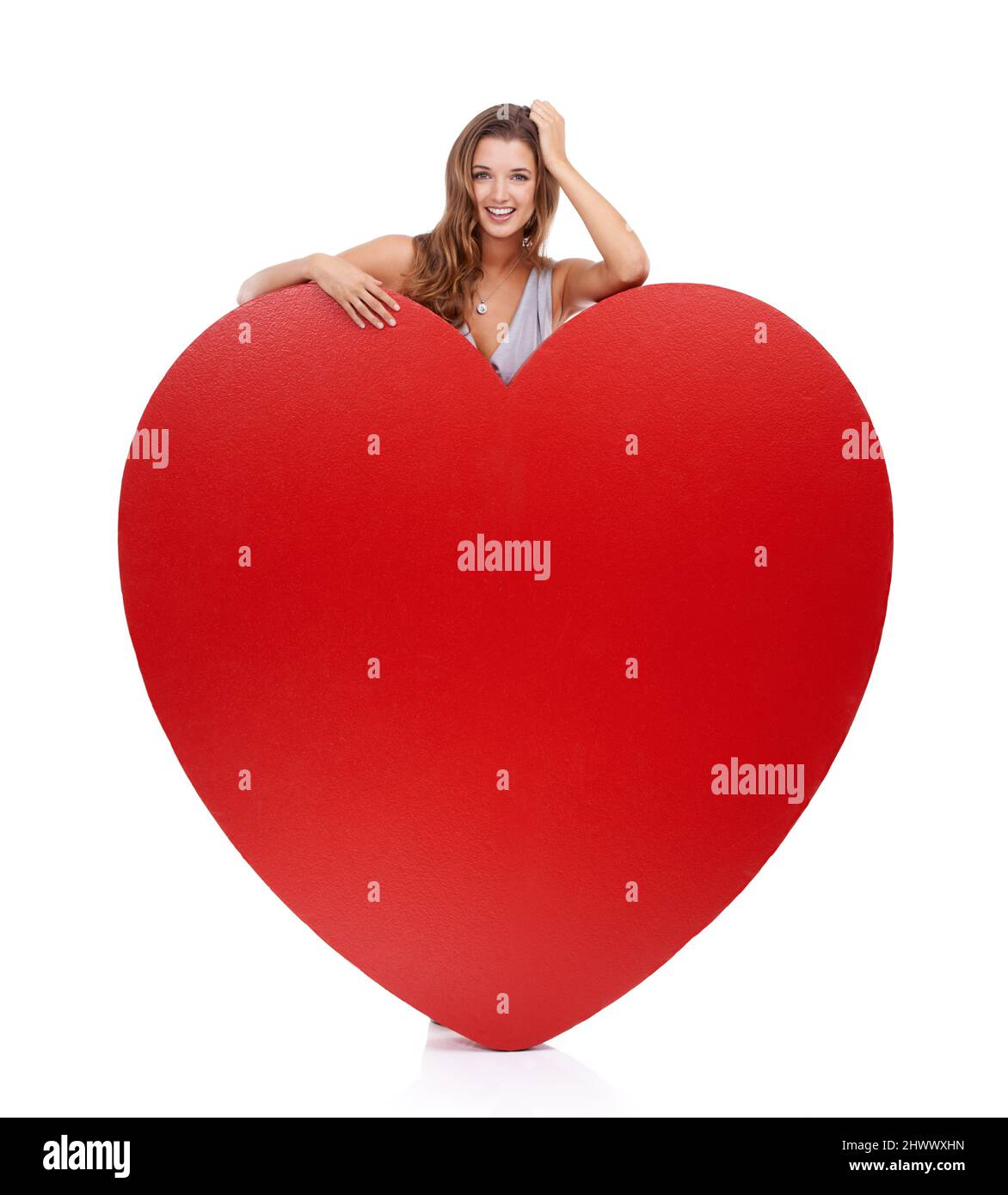 She has a lot love to give. Portrait of an attractive young woman standing behind a giant heart-shaped prop. Stock Photo