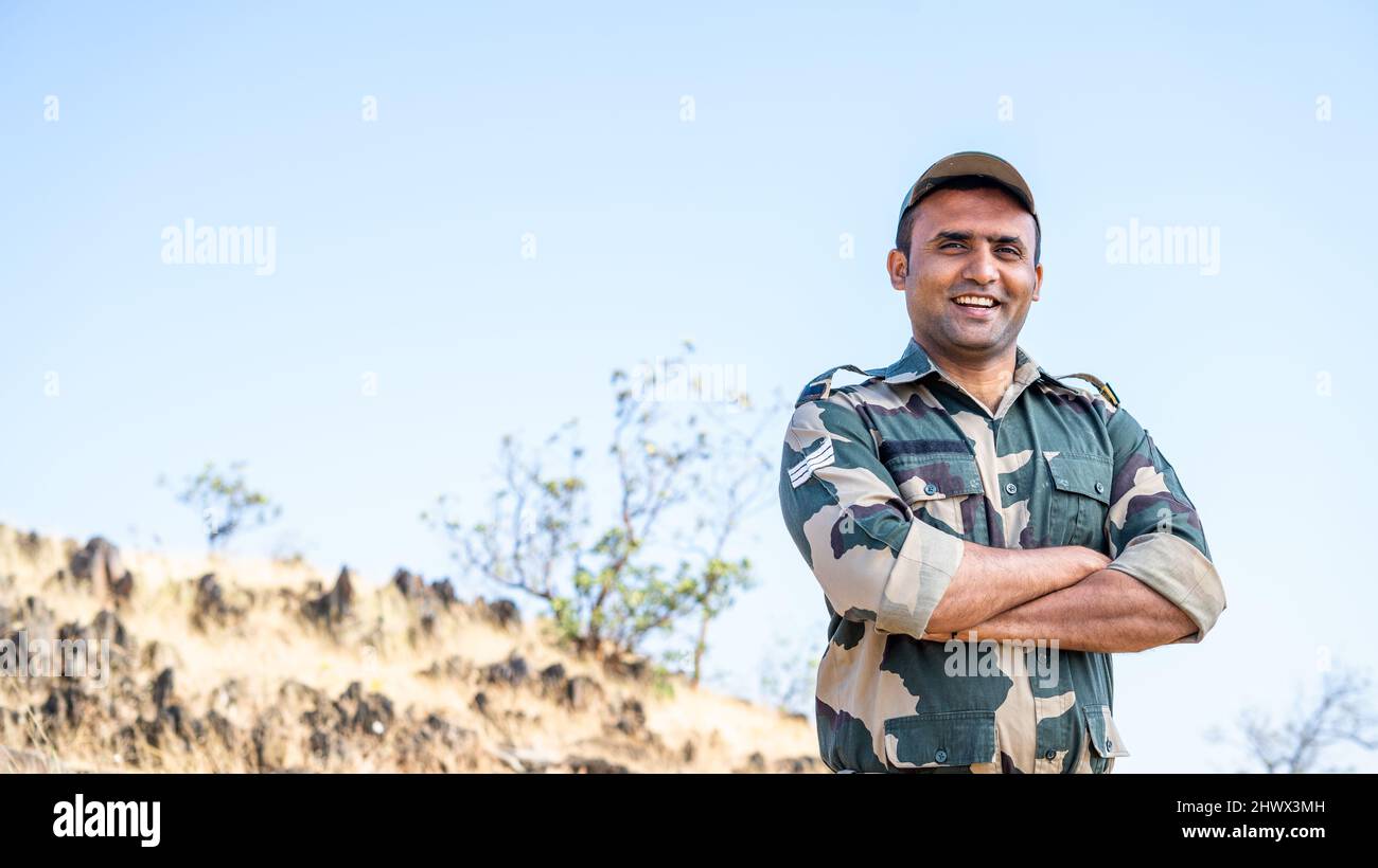 Confident smiling indian soldier in uniform standing with arms crossed by looking at camera - concept of successful, proud serviceman and occupation. Stock Photo