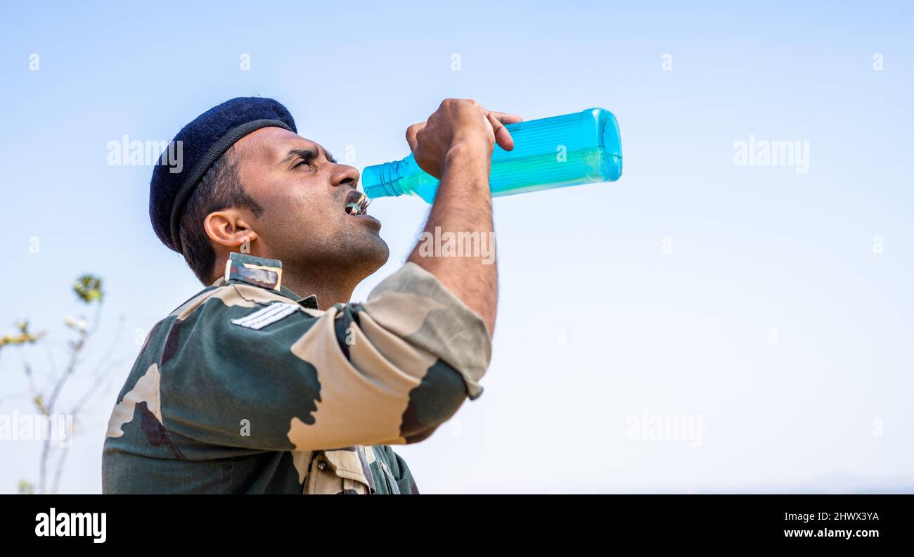 Thirsty solider drinking water while on top of mountain during hot sunny day - concept of taking break, relaxation and summer heat wave. Stock Photo