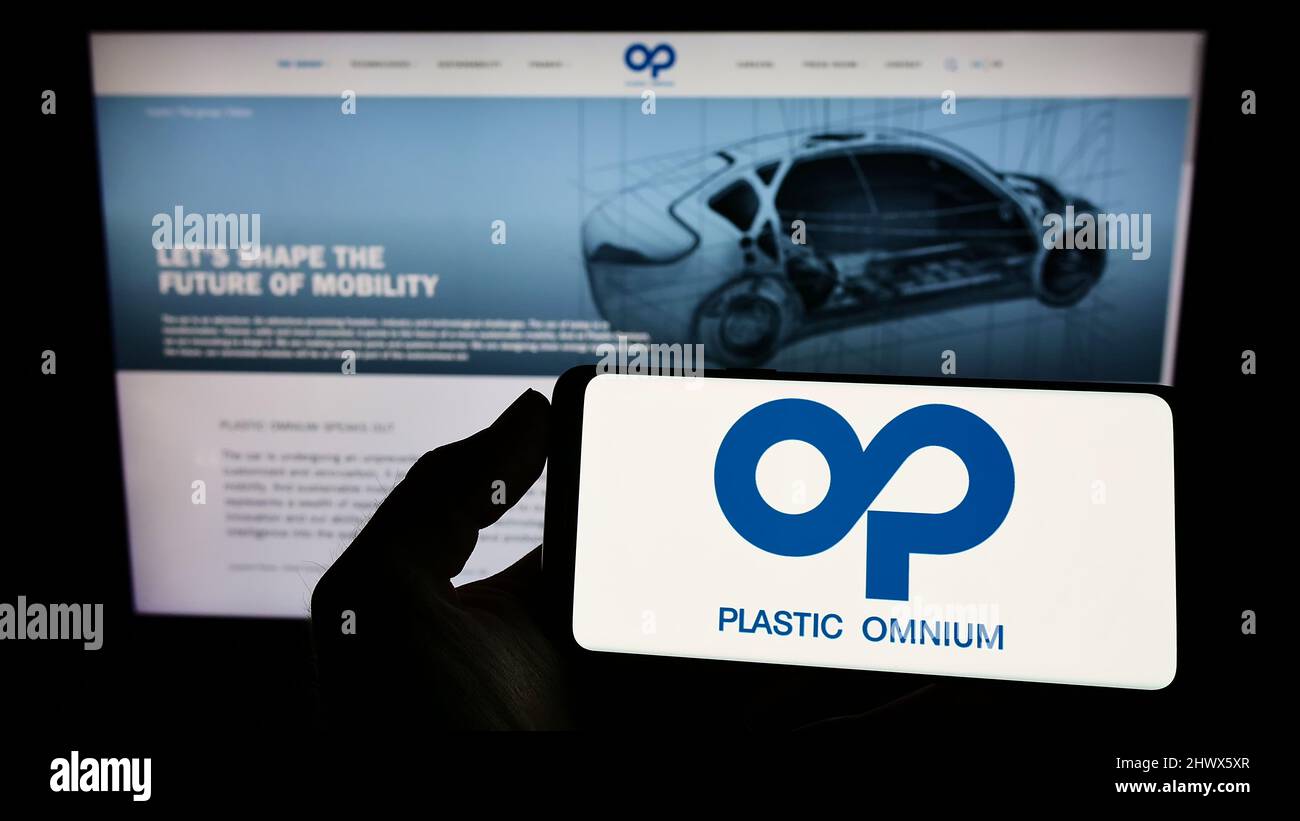 Person holding smartphone with logo of French company Compagnie Plastic Omnium SA on screen in front of website. Focus on phone display. Stock Photo