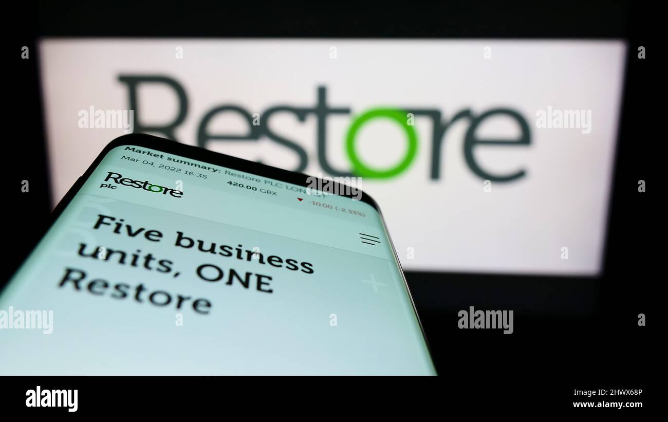 Smartphone with website of British data management company Restore plc on screen in front of business logo. Focus on top-left of phone display. Stock Photo