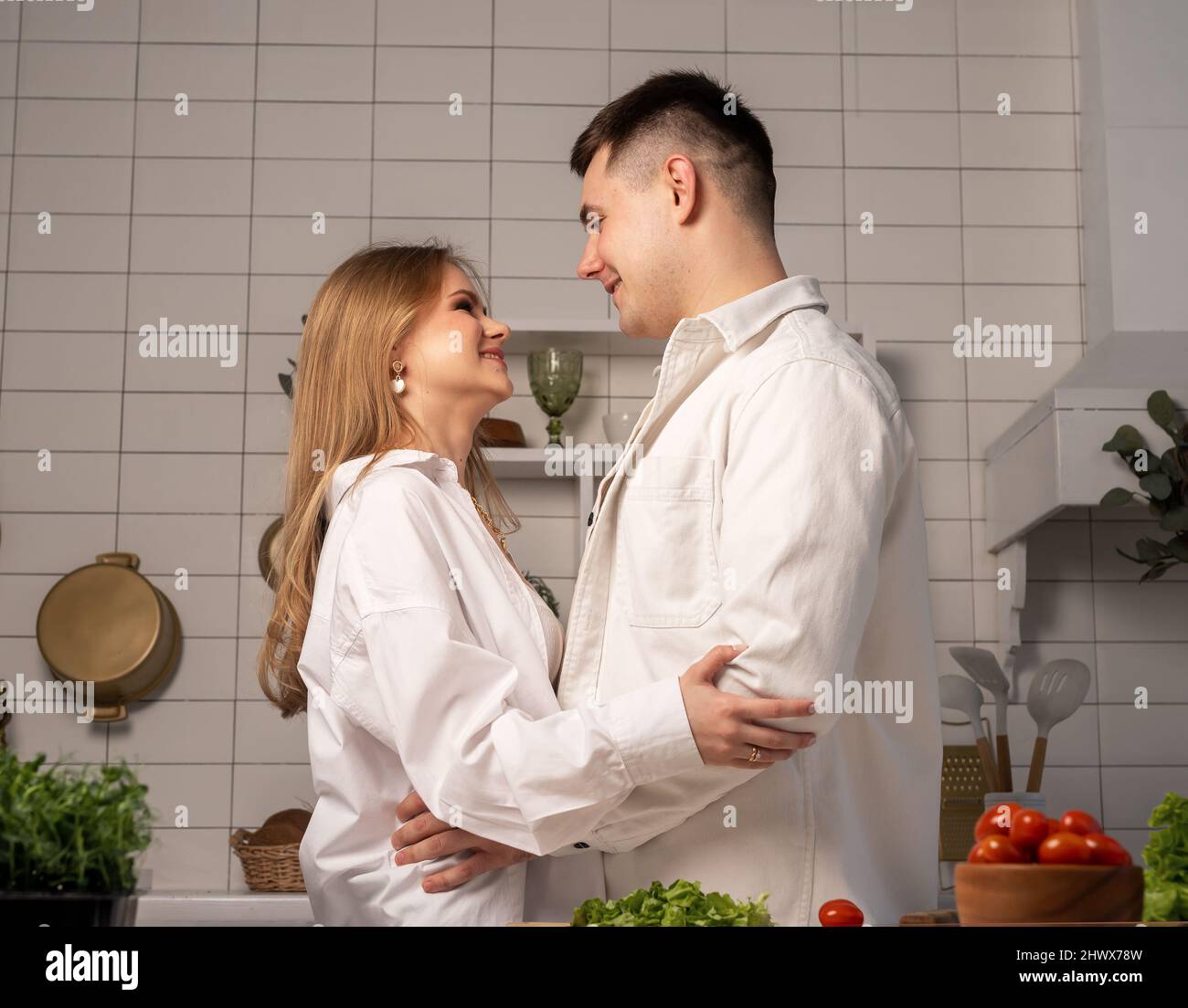 Happy young couple hugging while cooking at home. Handsome man and beautiful woman looking at each other with love. Romantic date. High quality photo Stock Photo