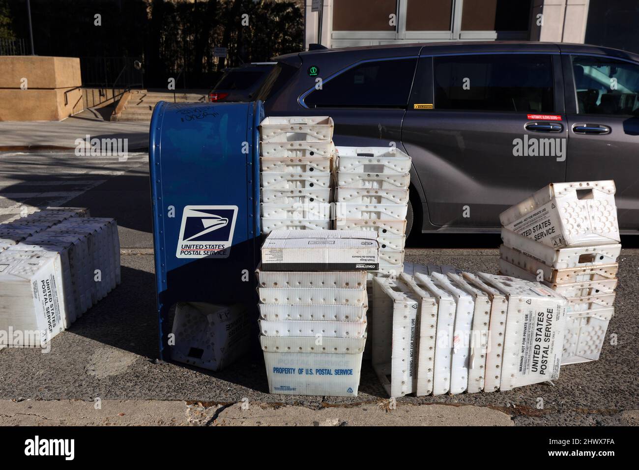 Large stacks of corrugated plastic flat tubs stacked next to a us postal service mailbox. plastic bins for the storage and transport of mail Stock Photo