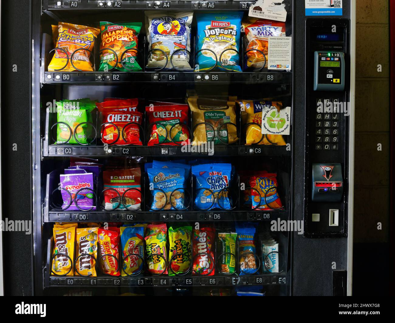 American snacks, chips, crisps, candy and other junk food in a vending machine with cashless, coin and card payment options. Stock Photo