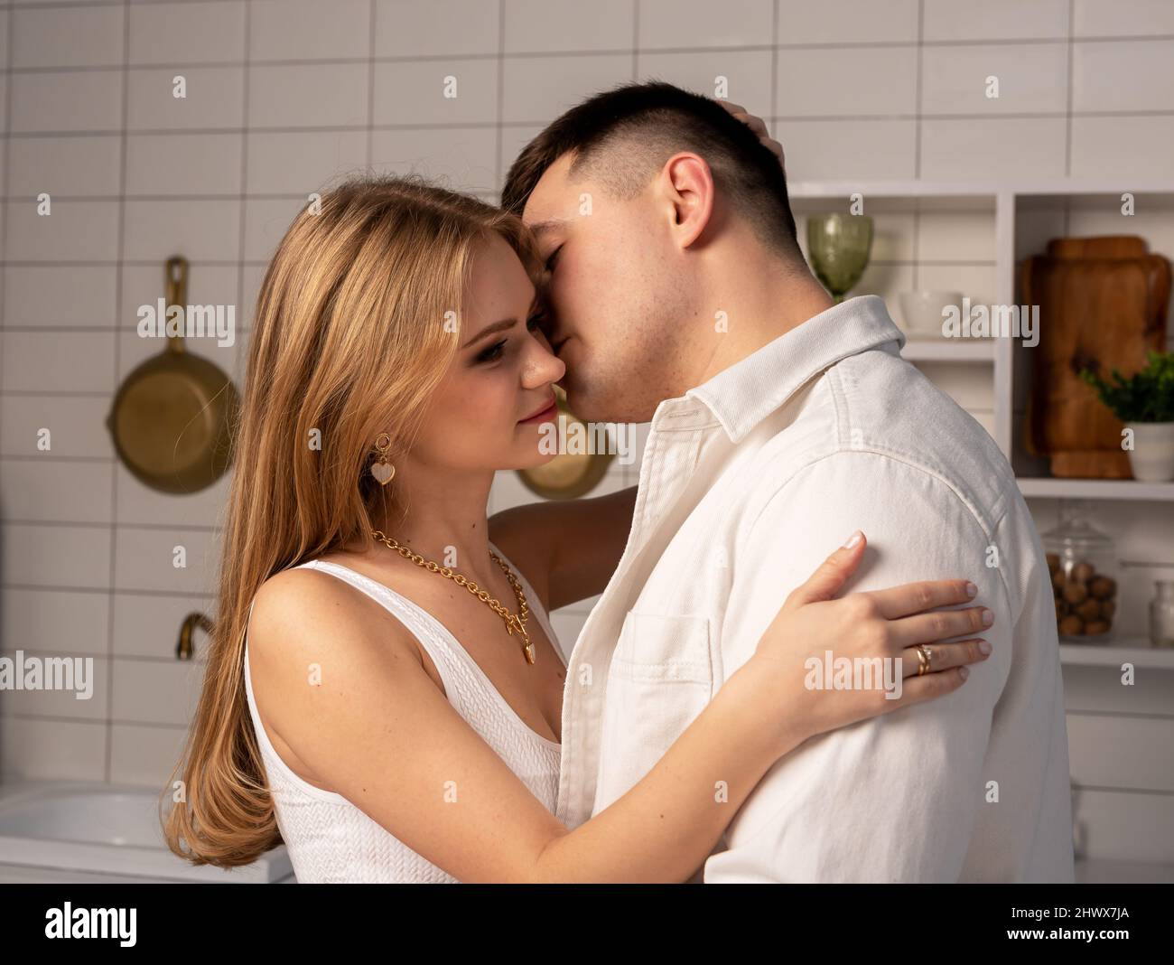 Handsome man kissing wife in cheek in kitchen. Happy young couple hugging while cooking at home. High quality photo Stock Photo