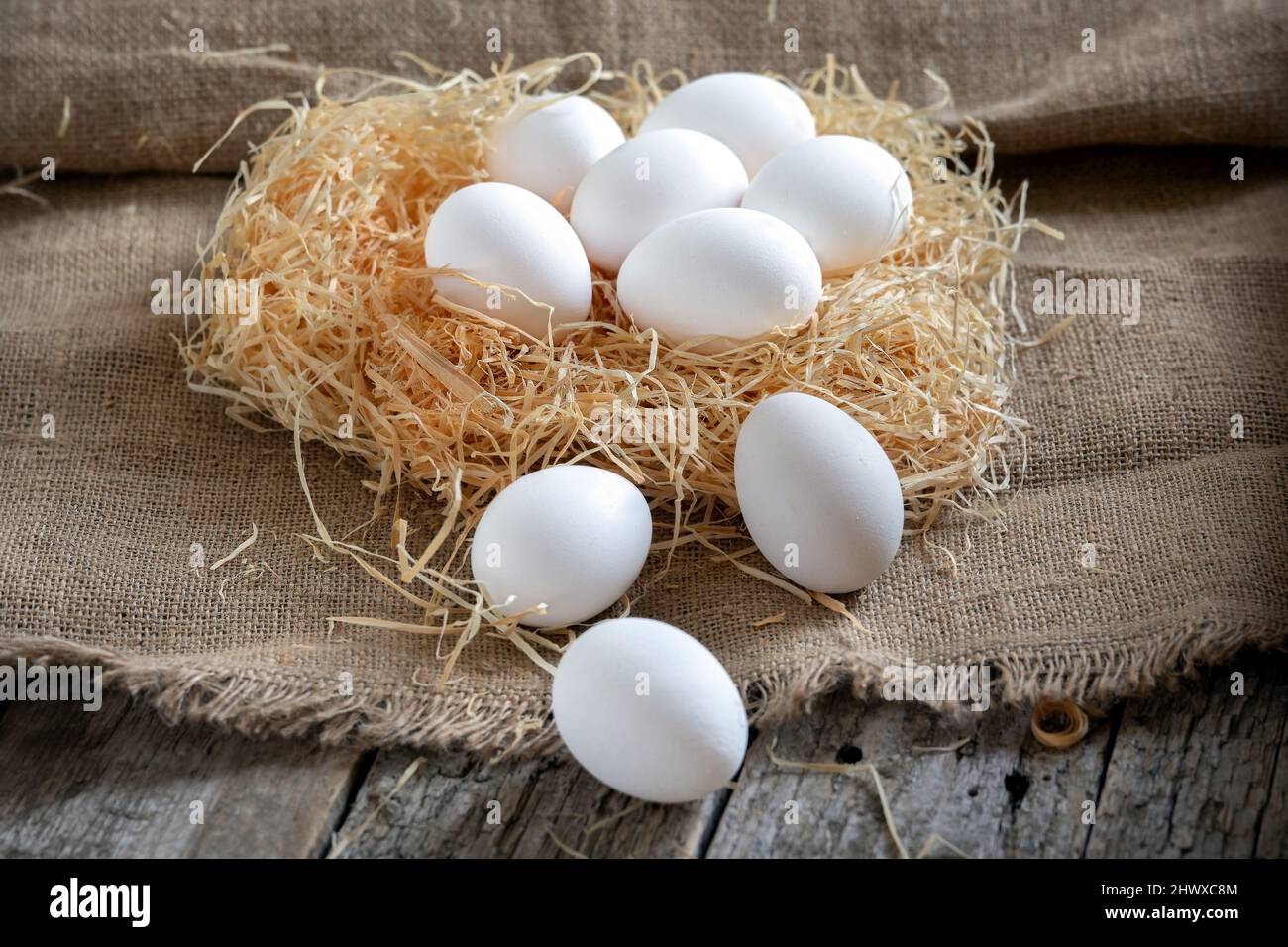 White chicken eggs in the straw nest on a burlap on wooden boards Stock ...
