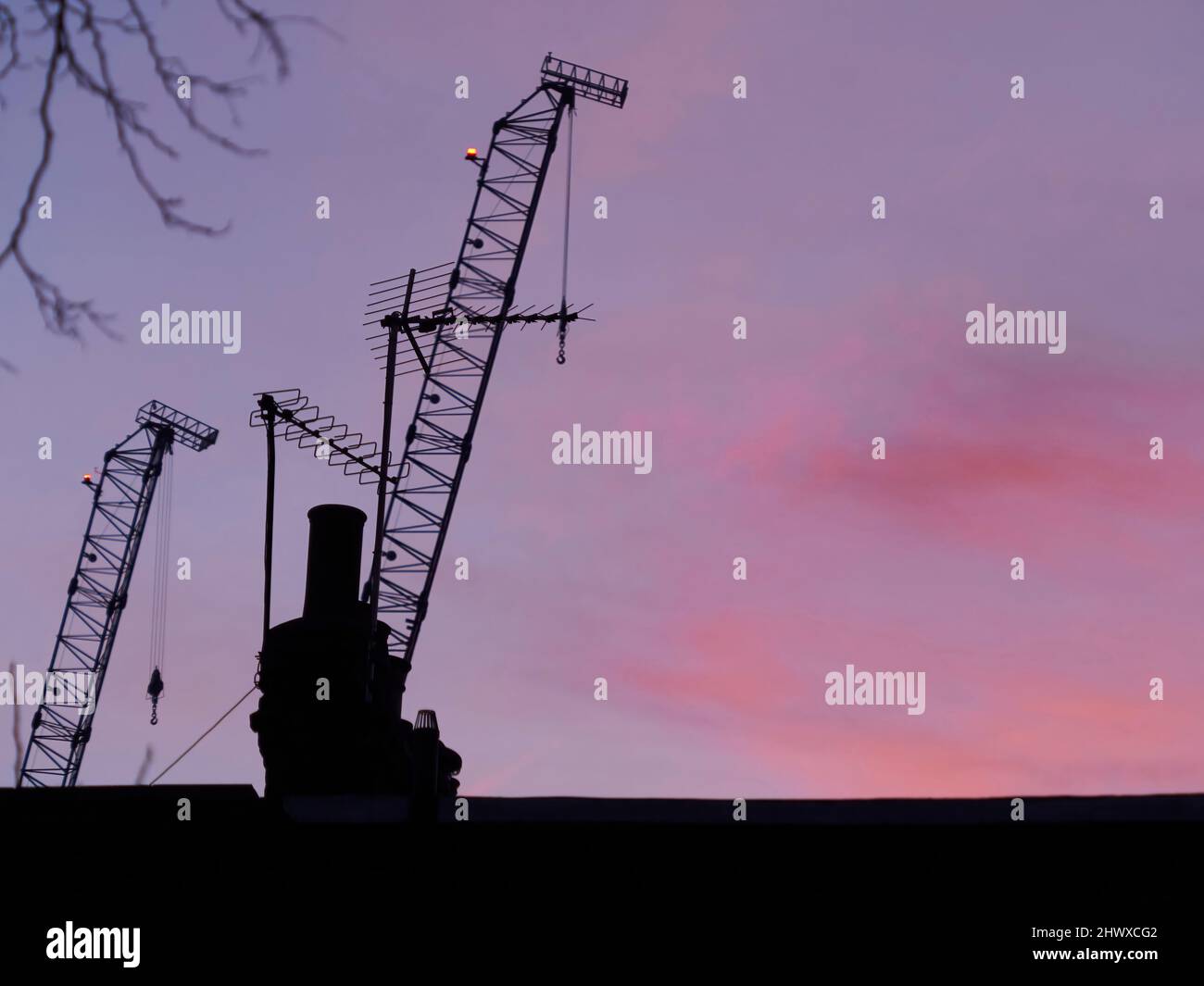 A vibrant, rich dawn over London, with cranes, chimney pots and aerials silhouetted against a purple, pink and red sky. Stock Photo
