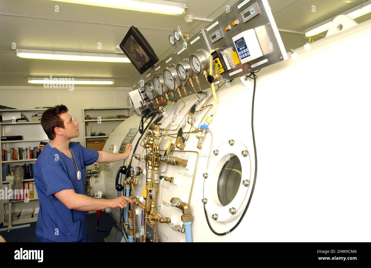 A hyperbaric technologist monitors a patient in the chamber, through a monitor as there are various cameras within the chamber. The technologist will Stock Photo