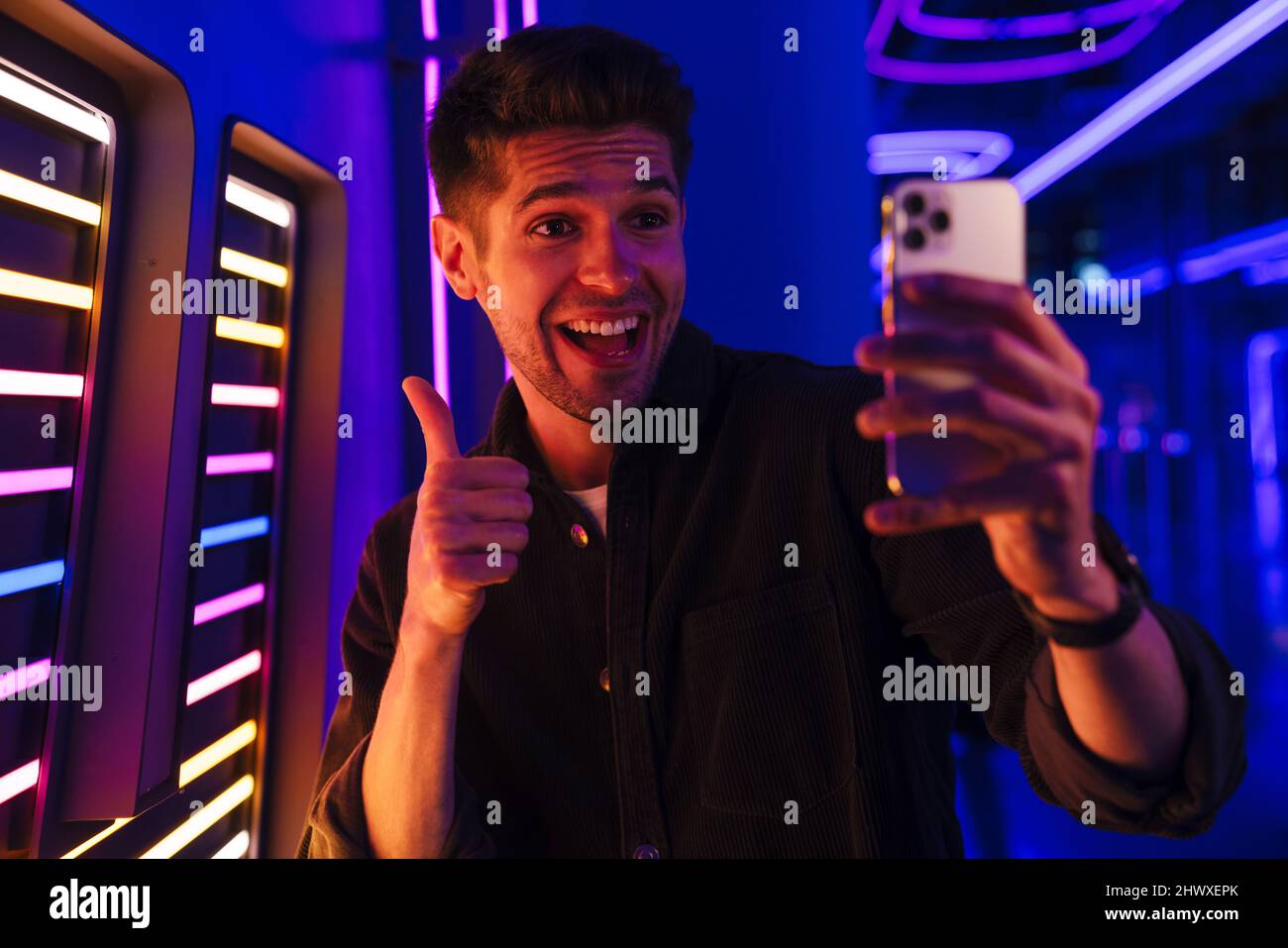 Young bristle man showing thumb up while taking selfie on mobile phone indoors Stock Photo