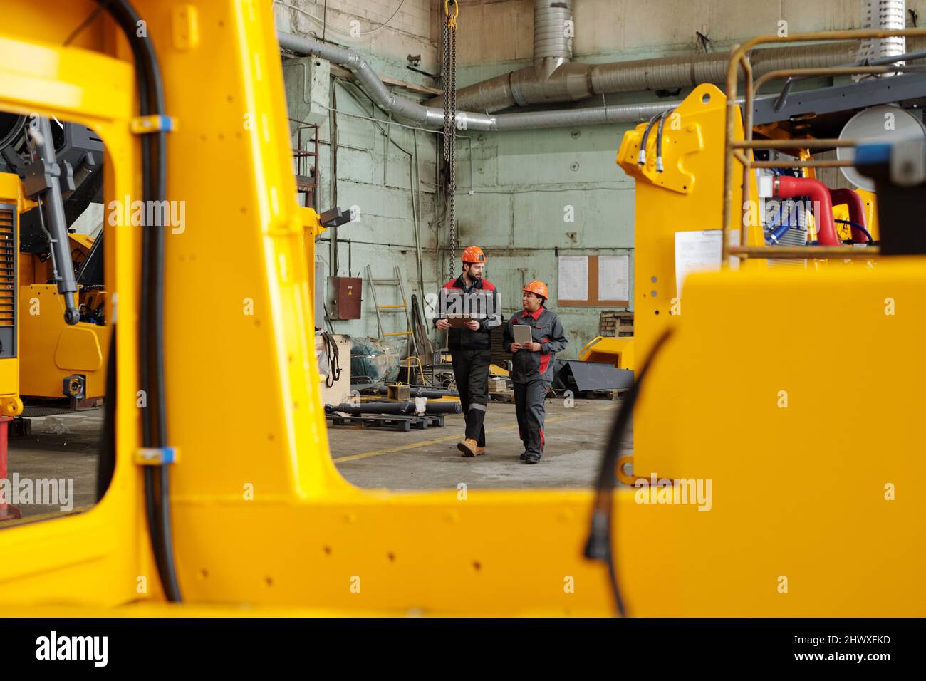 Two workers of large industrial plant moving along warehouse or ...