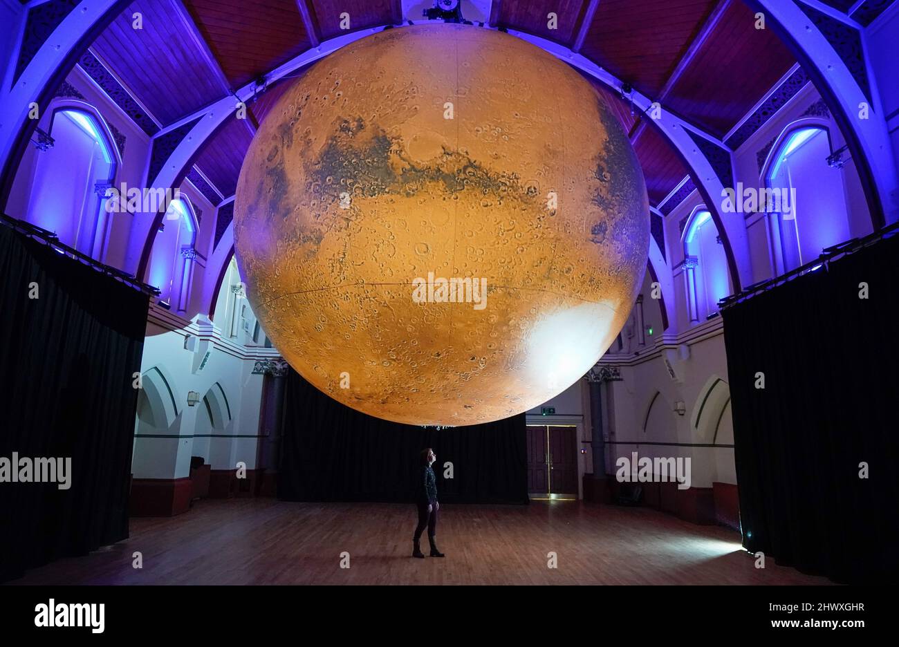A person looks up at Luke Jerram's seven-metre diameter artwork Mars, as it goes on display at the Corn Exchange, Dorchester. Picture date: Tuesday March 8, 2022. Stock Photo