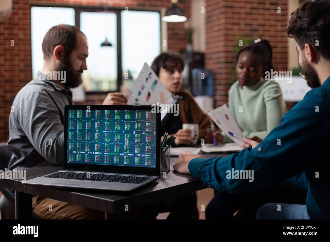  A group of businesspeople are sitting around a table looking at a laptop screen with financial data on it.