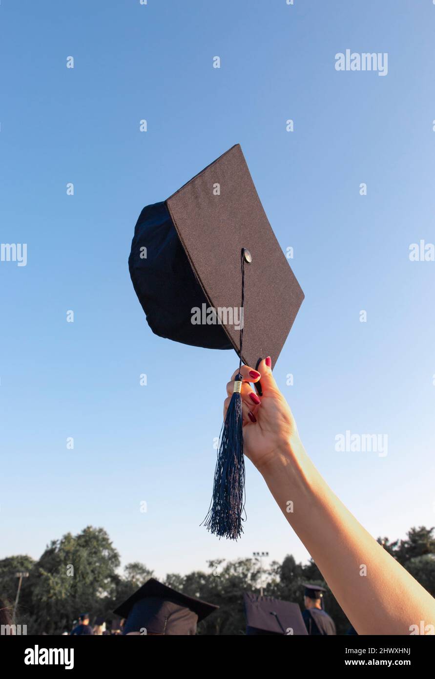 Graduation cap is holding up to the blue sky. The concept of proud, honour, success. Stock Photo