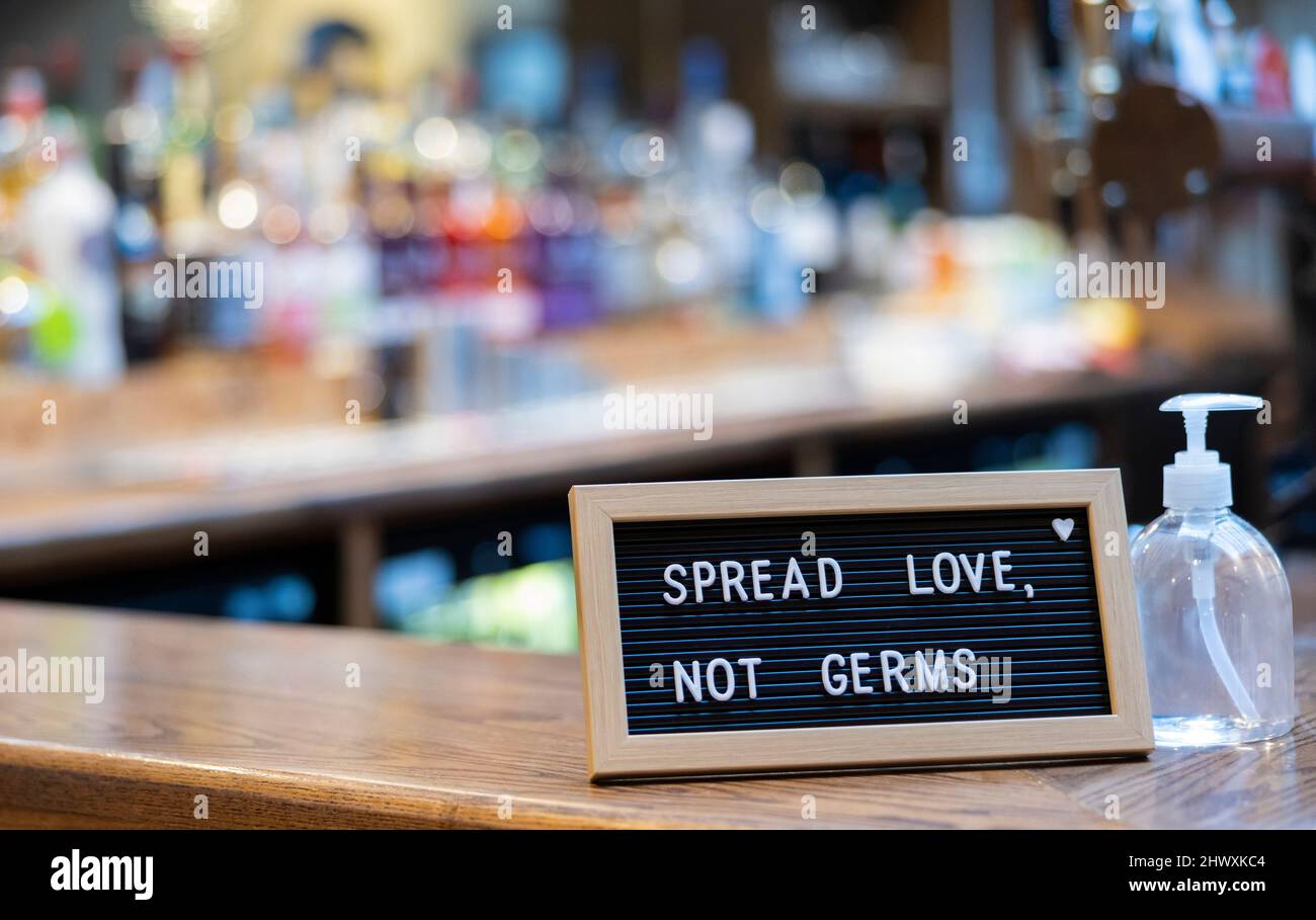 Spread Love Not Germs Sign Next To Hand Sanitiser Bottle On Bar Counter Stock Photo