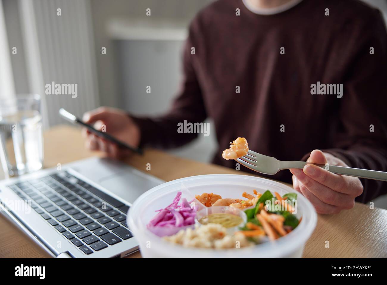 Close Of Man Eating Healthy Lunch At Office Deak Whilst Using Laptop Stock Photo