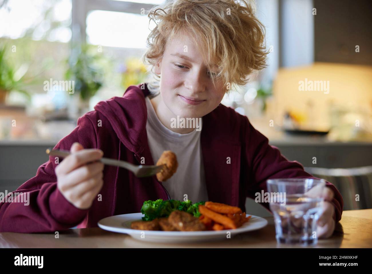 Teeange Girl Eating Vegan Meal Sitting At Table In Kitchen At Home Stock Photo