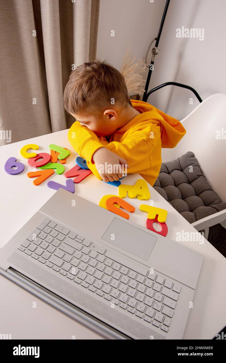 Little boy learning alphabet and numbers online, with laptop at home. Child is sad and tired. Negative emotions, stress, mental problems Stock Photo