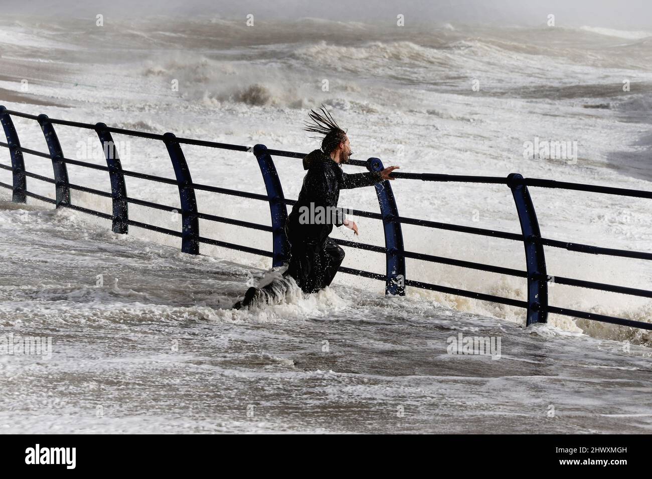 England, East Sussex, Hastings, Man braving the wild waves battering the promenade during storm. Stock Photo