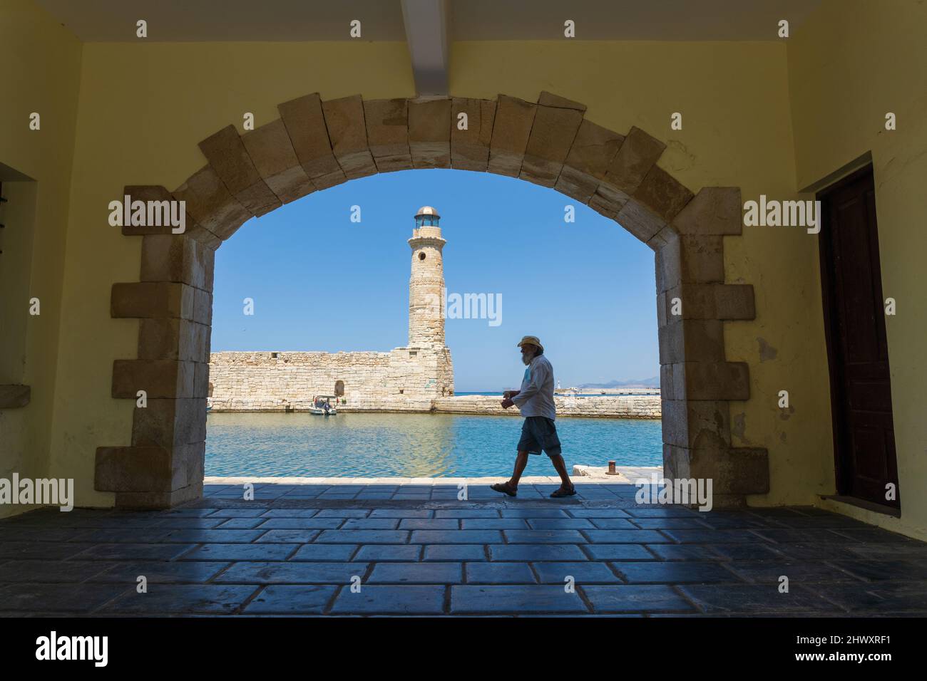 Rethymno, Crete, Greece - June the 30th, 2021: Person walking along the cost of Rethymno, the light house in the background Stock Photo