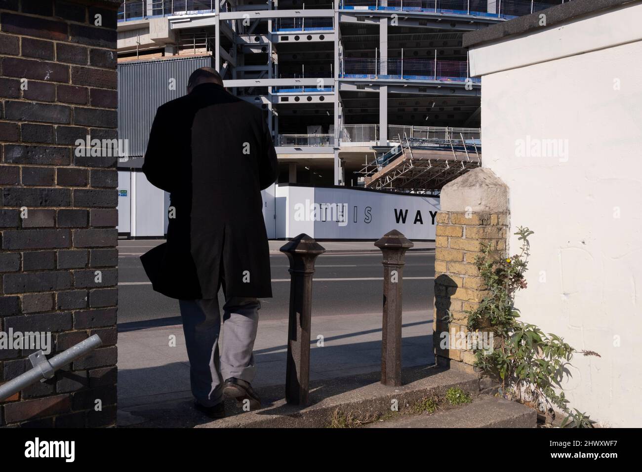 A pedestrian passes through a gap bteen old walls opposite new properties at the redeveloped Battersea Power Station in Nine Elms, on 7th March 2022, in London, England. Stock Photo