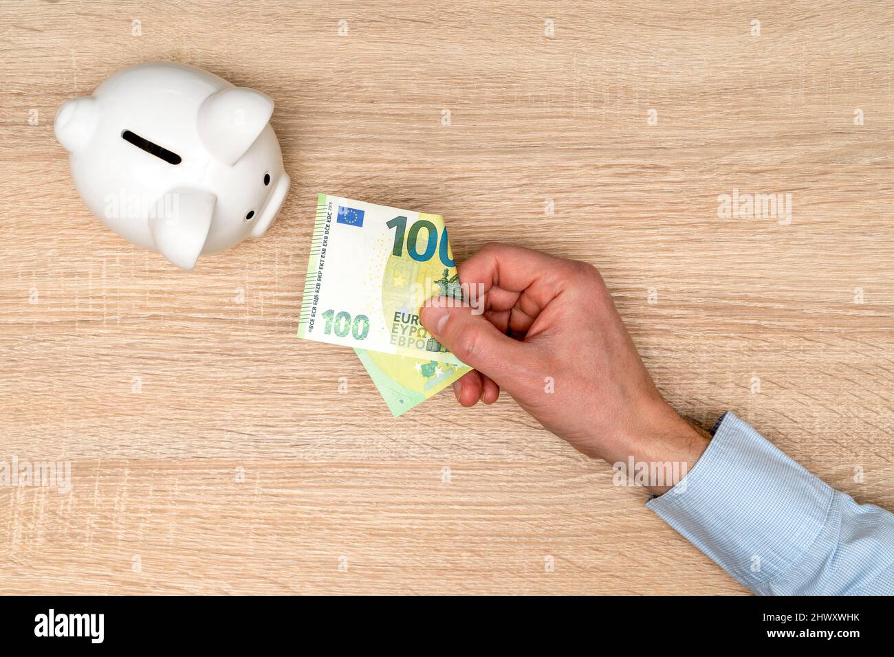 Hand Putting One Hundred Euros in Piggy Bank. Savings Concept. Stock Photo