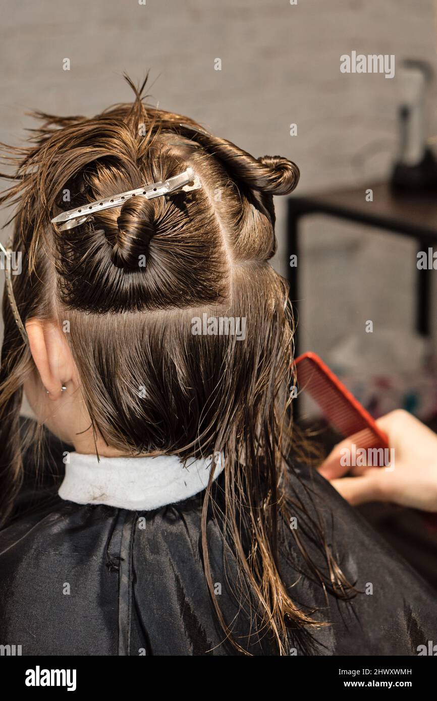 Hand of hairdresser doing haircut of kid with hair clips on her hair in