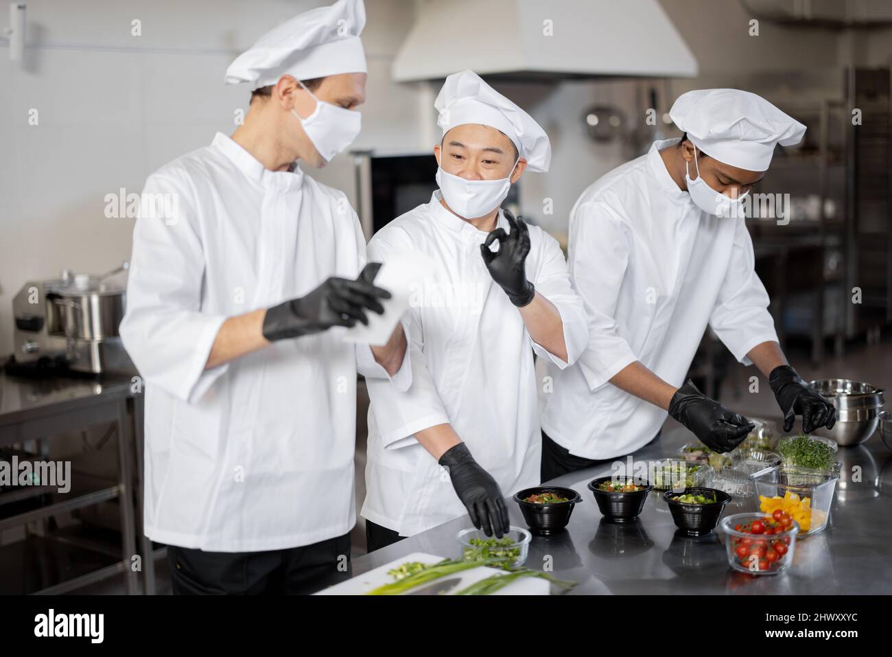 Three well dressed chefs in face masks prepare takeaway food in ...