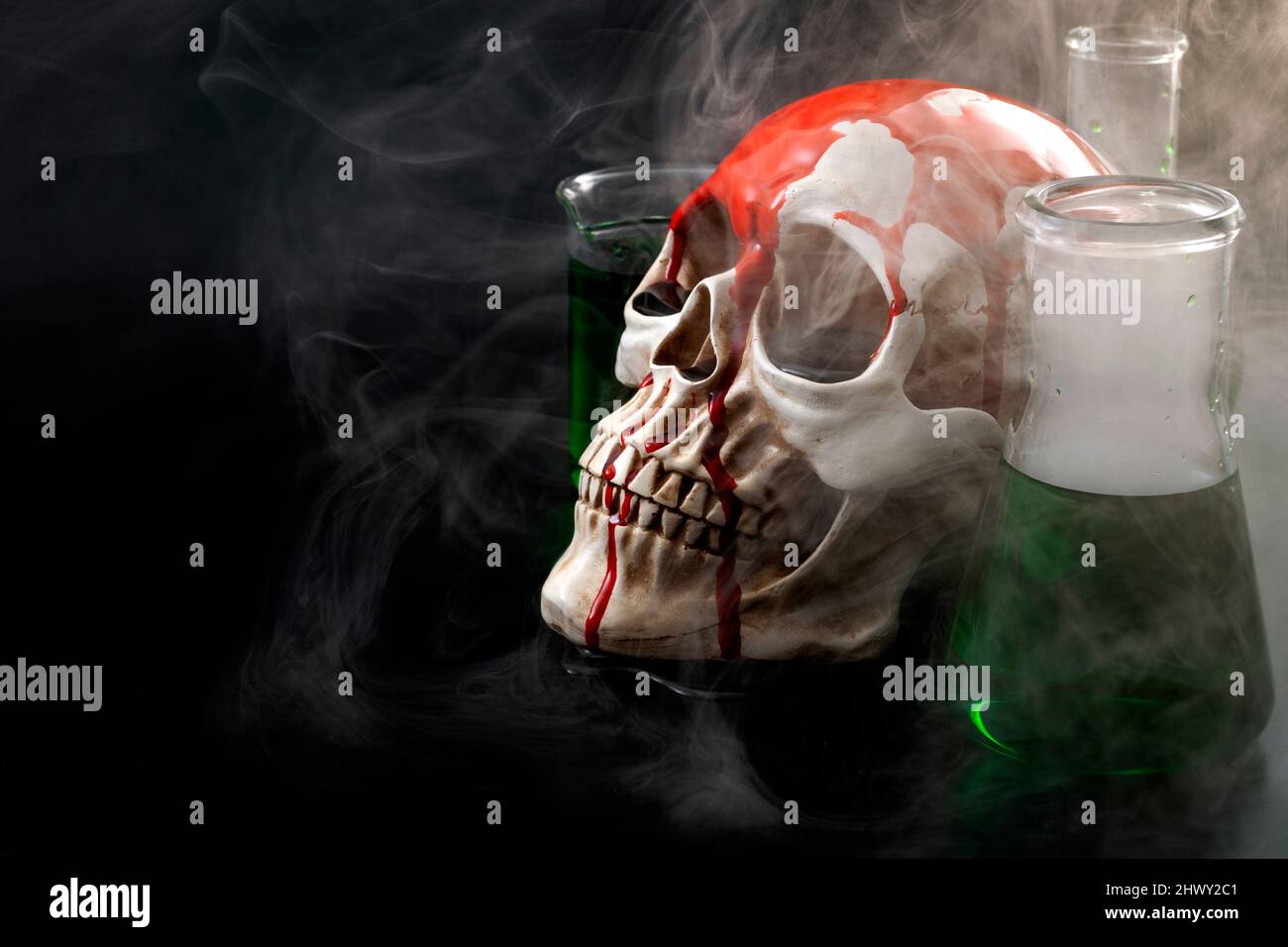 Biological warfare, chemical attack and genocide concept with a skull surrounded by chemistry flasks with smoke or mustard gas coming out of the green Stock Photo