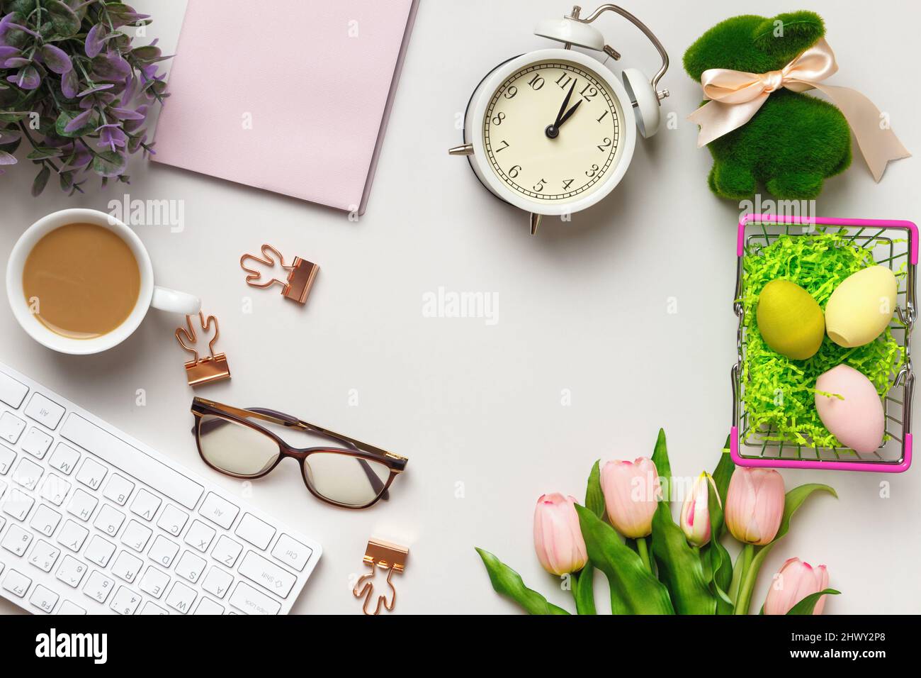 Desktop. Glasses coffee cup notepad on keyboard alarm clock on table with easter decorations. Stock Photo