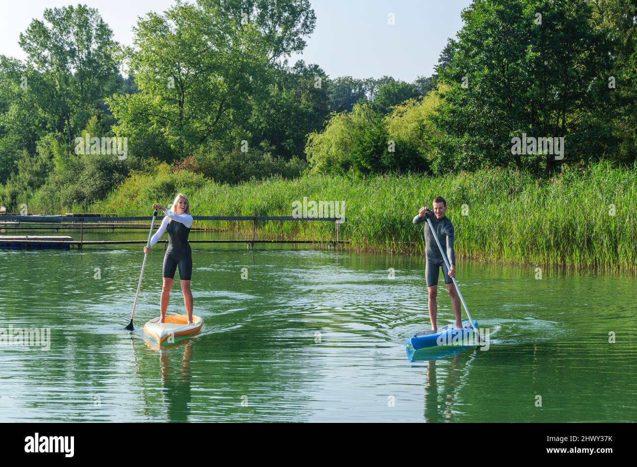 Two young people having fun while paddling with a SUP board on a lake ...