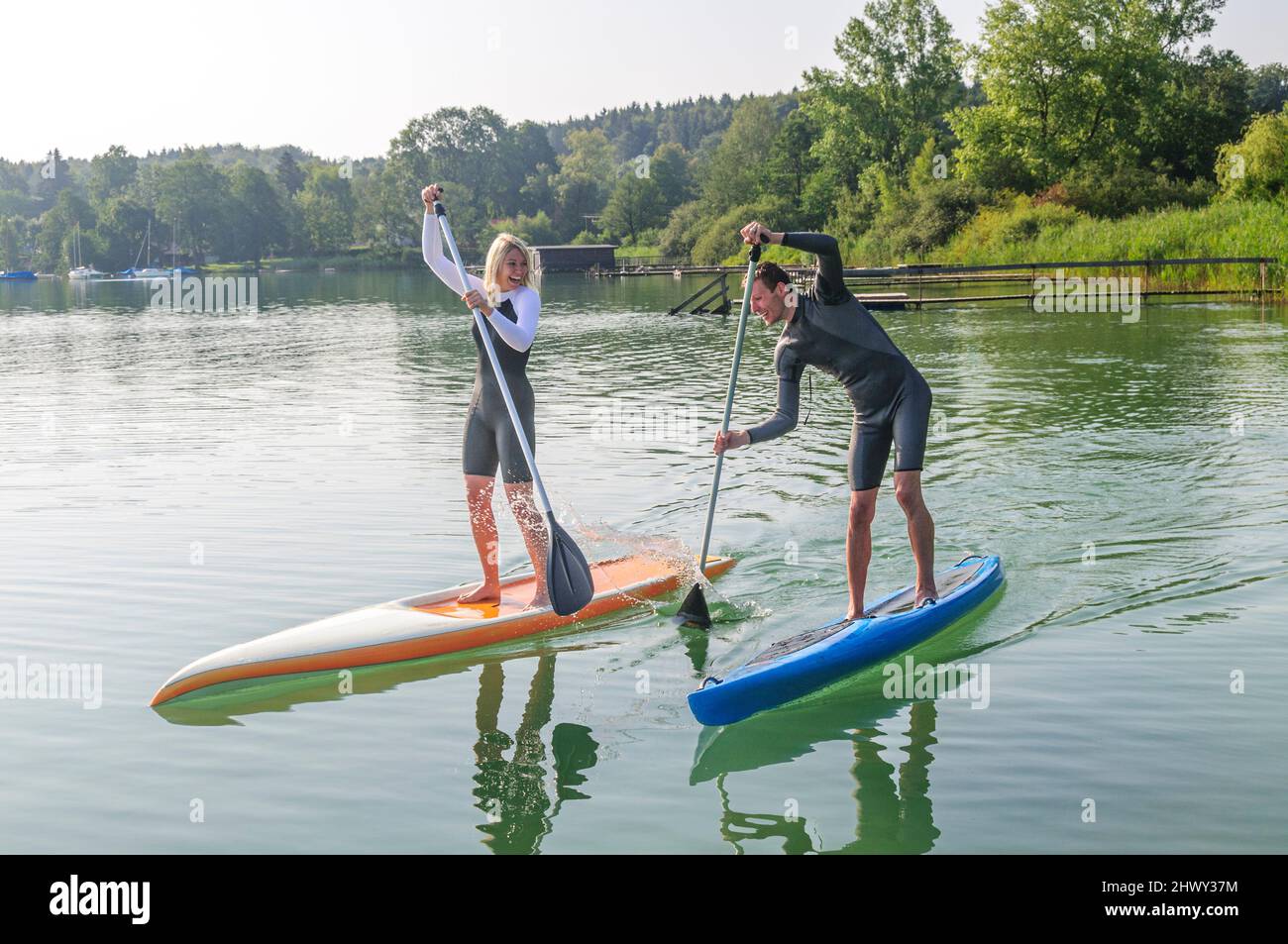 Two young people having fun while paddling with a SUP board on a lake ...