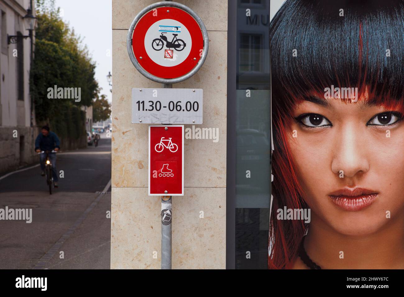 Cyclist related signage, a shopfront advertisement and a cyclist in a lane. Solothurn, Switzerland. Stock Photo