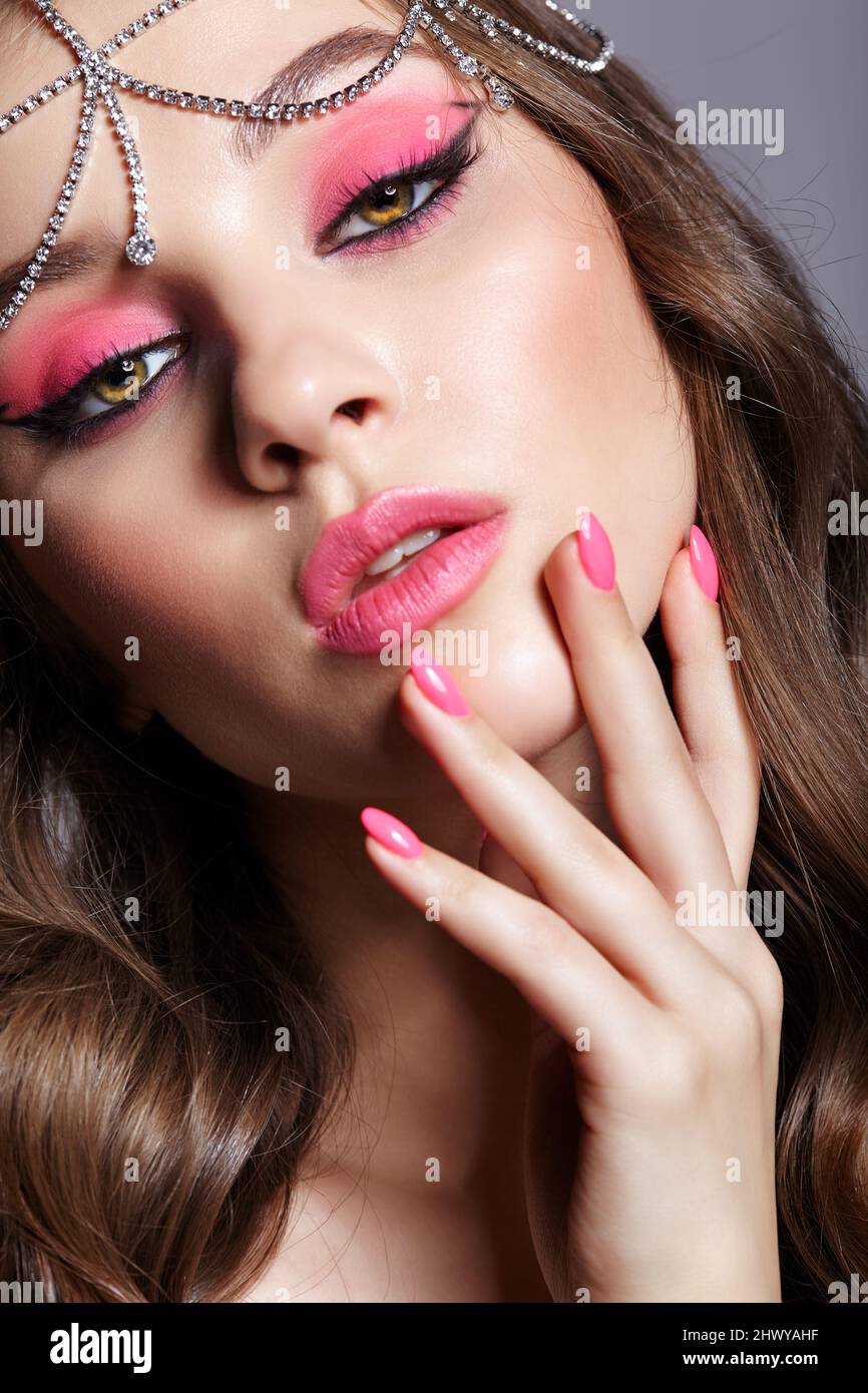 Beauty portrait of young woman with hand near face. Brunette girl with an oriental appearance with pink makeup and rhinestone embellishment on the hea Stock Photo