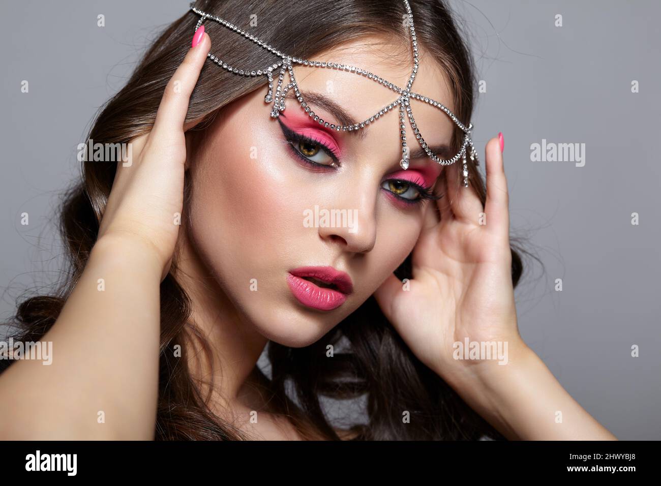 Beauty portrait of young woman with hands near face. Brunette girl with an oriental appearance with pink makeup and rhinestone embellishment on the he Stock Photo